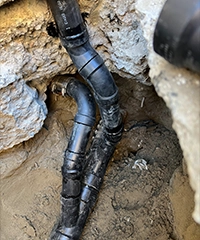Plumber repairing plumbing beneath a kitchen sink while homeowner stands nearby watching